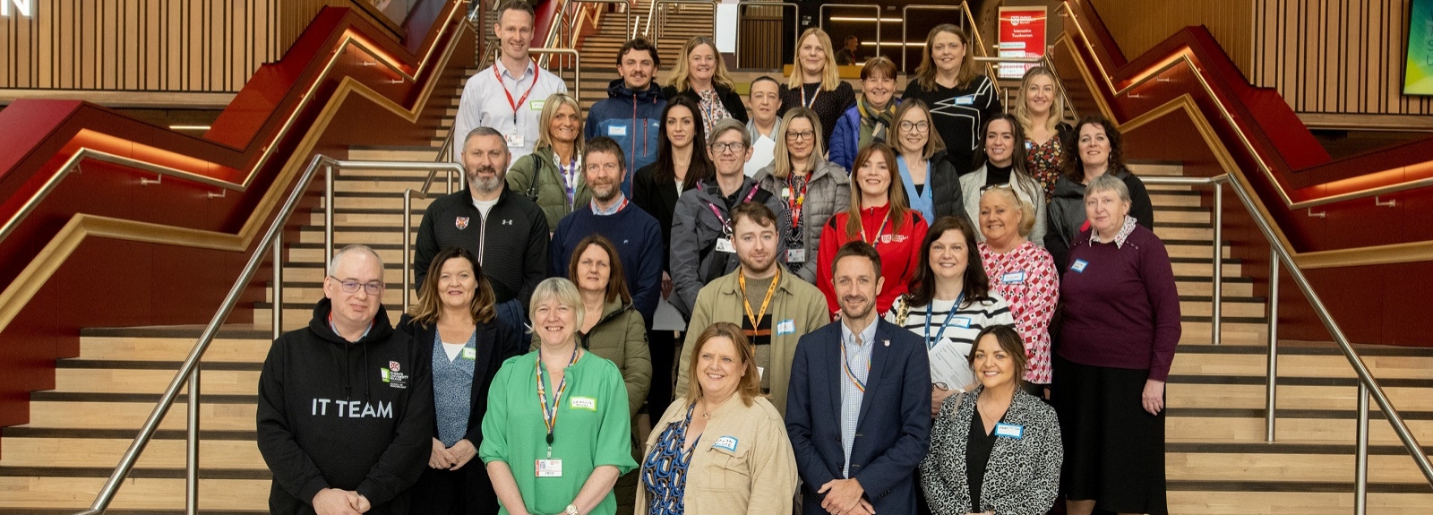 Group photo of Queen’s University Belfast staff and participants gathered on a staircase inside a university building, taken during an Inclusive Employment Scheme event.
