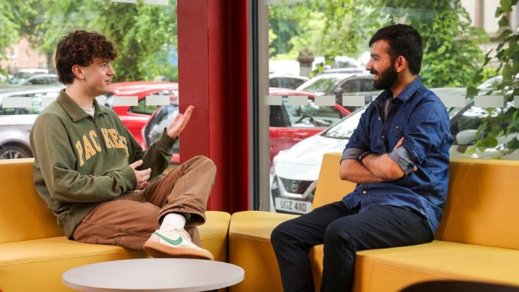 two male student sitting chatting in university building