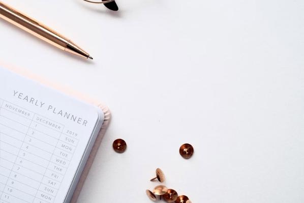 A year planner, tacks and a pen lay on a table.