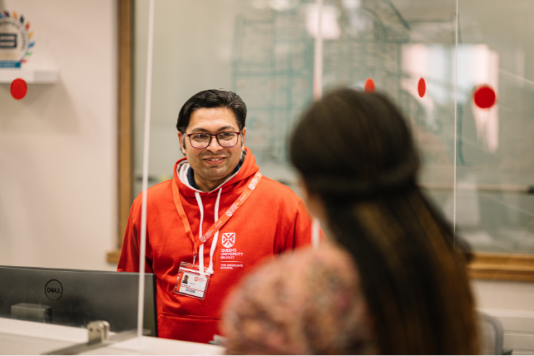 Image shows a student assistant answering a query at a reception desk.