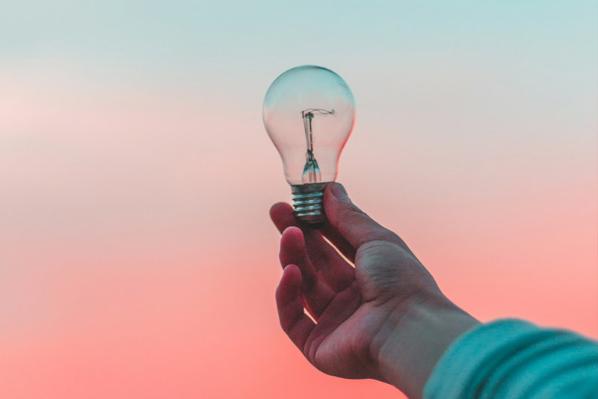 A person holds a bulb to the blue-pink gradient sky.