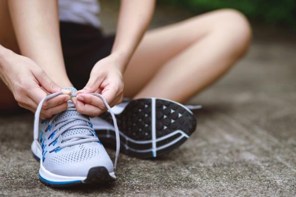 A man tying the laces of a pair of running shoes while sitting on the ground.
