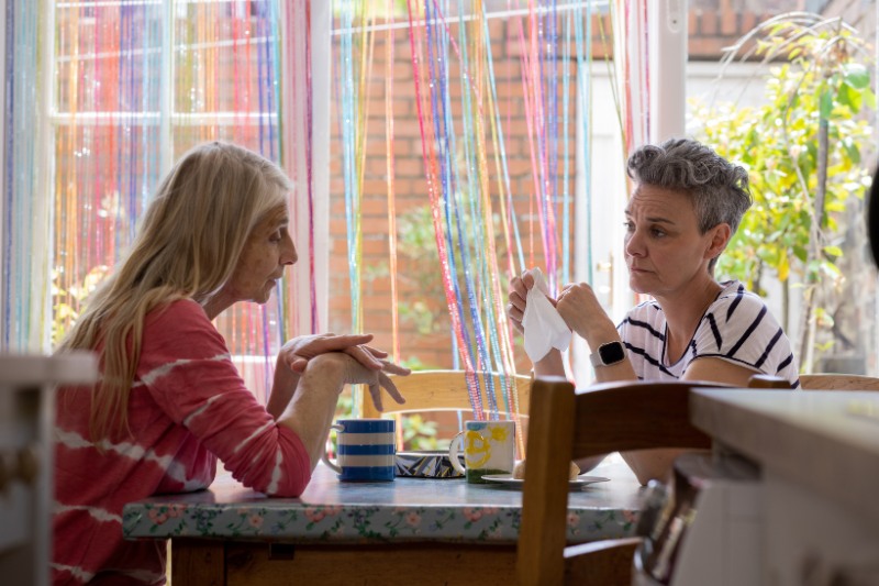 two mature women talking at a table over a hot drink