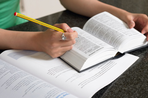 Person writing in a book with a yellow and black pencil