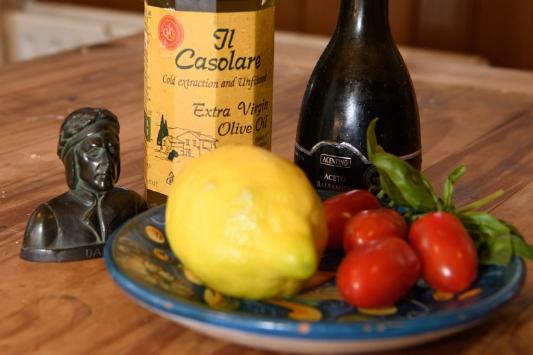 A bottle of Olive Oil, an Italian sculture and a plate of lemons and vine tomatoes on a wooden kitchen table