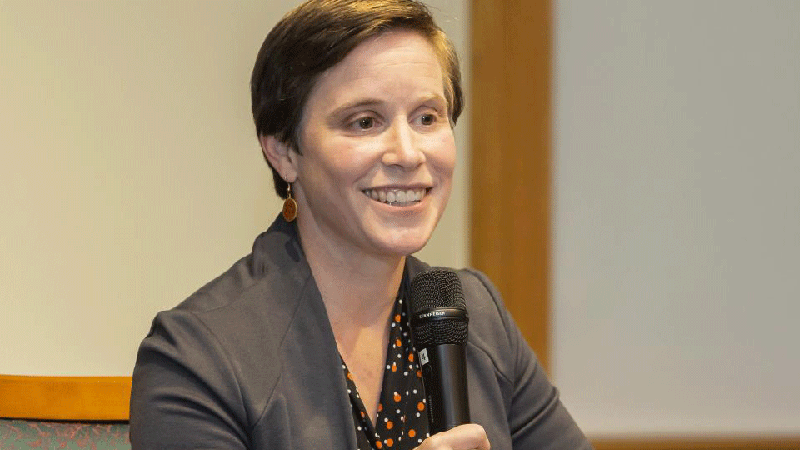 Dr Karen Ross speaking at an event, holding a microphone and smiling.