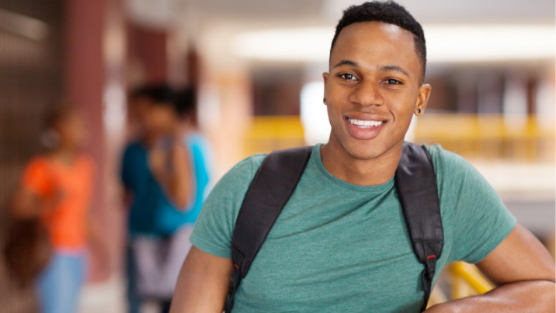 male student wearing a backpack standing looking at camera and smiling