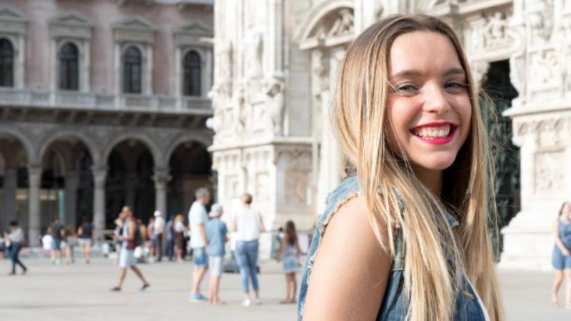 Female student standing outside in a town in Europe smiling to camera