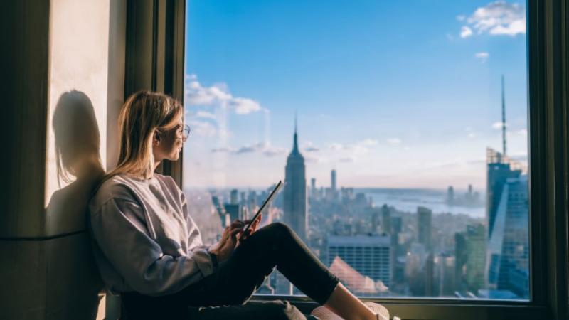 female student sitting in an apartment looking out at the view in the US