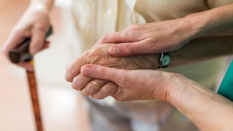 two hands supporting an elderly person on walking stick