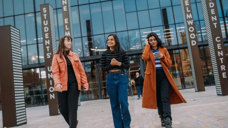 three female students walking away from the student centre at Queens