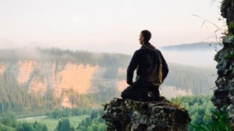 man sitting on the edge of a mountain looking at view