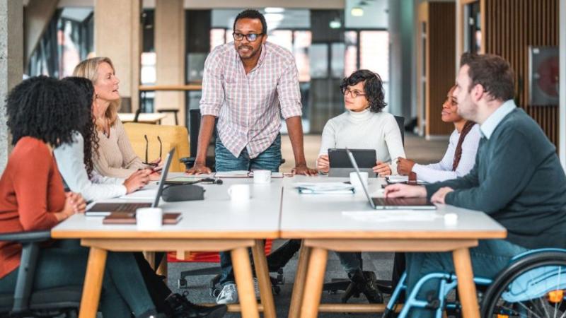 people sitting around a table in office environment chatting, one person is in a wheelchair