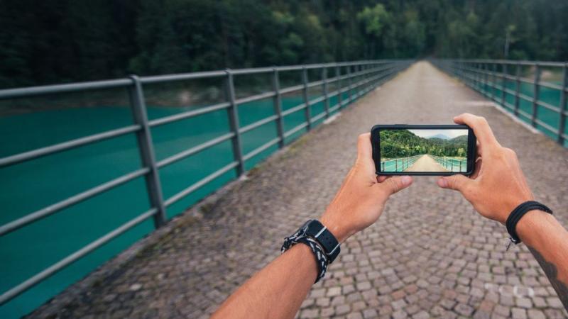 someone taking a photo on a mobile phone on a bridge over a river