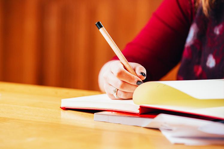 close up of a hand holding a pencil and making notes in a red notebook