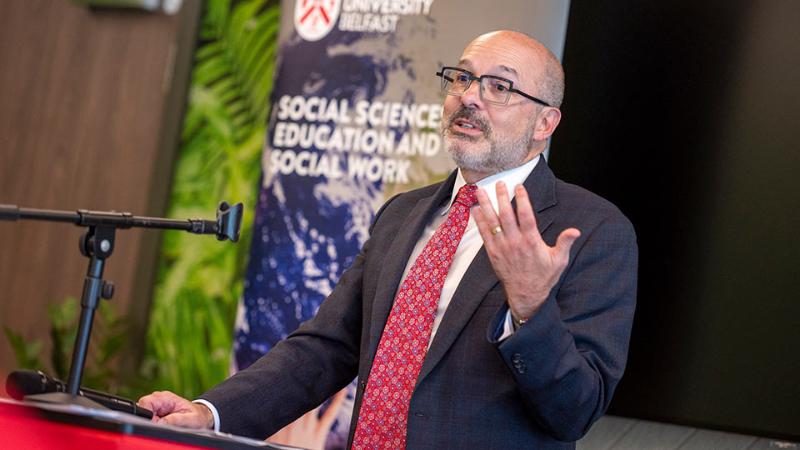 a man in glasses wearing a dark suit and red tie