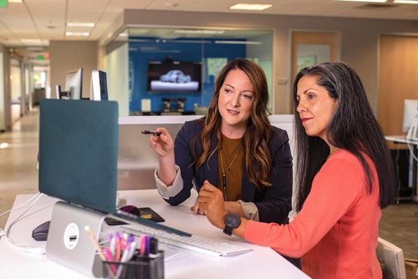 Two female professionals look at a laptop