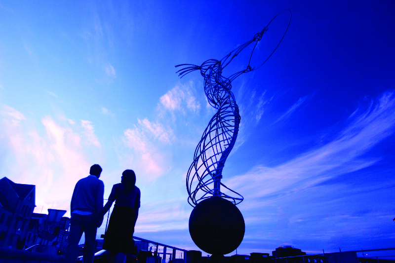 Two people looking upon the Beacon of Hope statue against an clear blue sky