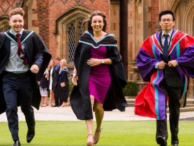 3 students in graduation outfits running over lawn