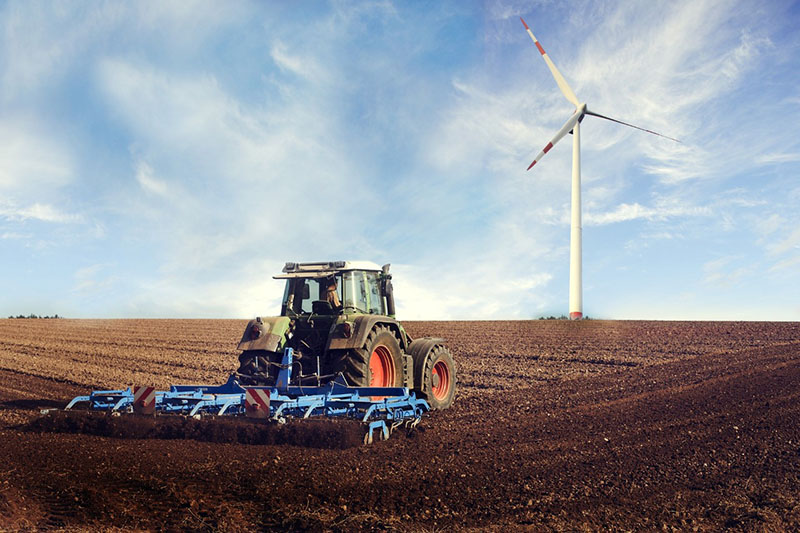 Tractor in a field with a wind turbine in the background