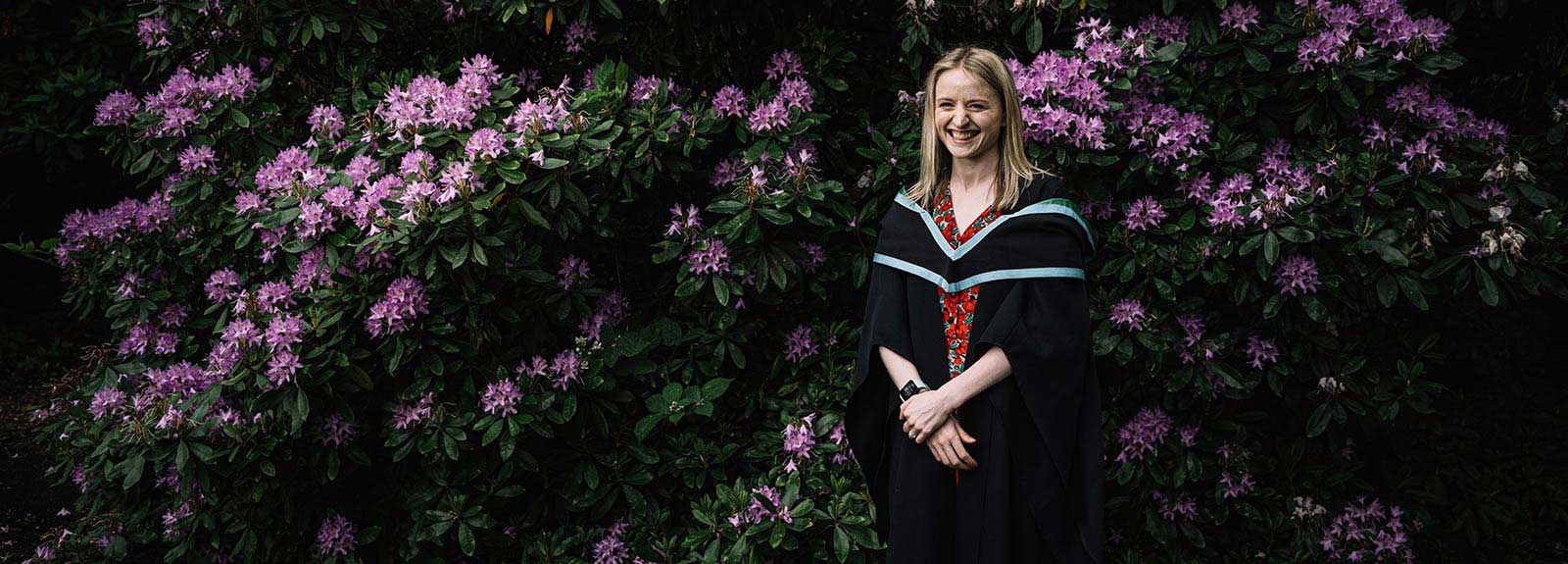 Graduating student in gown in front of flowers