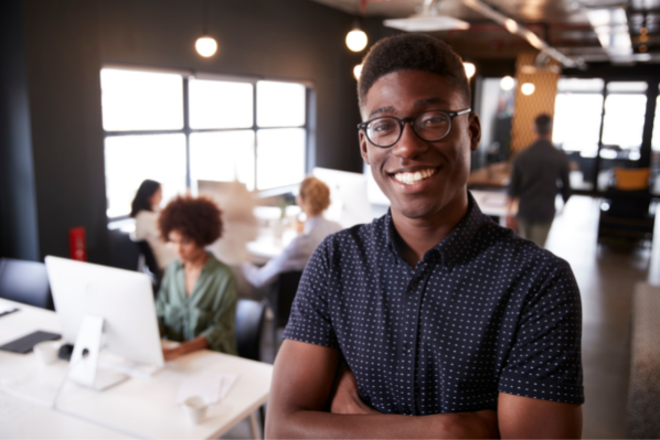 black male standing smiling to camera with arms folded in an office environment