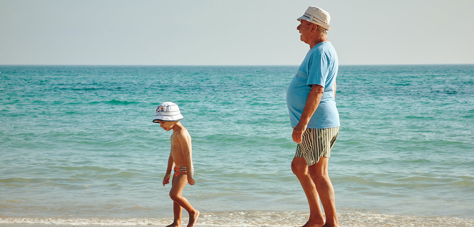 Man walks behind a child on a beach