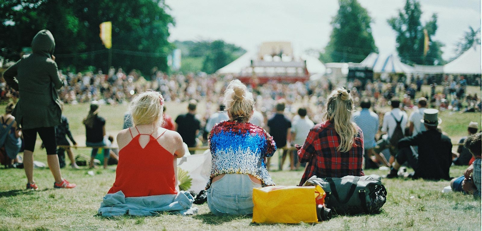 three girls sit on grass at a concert