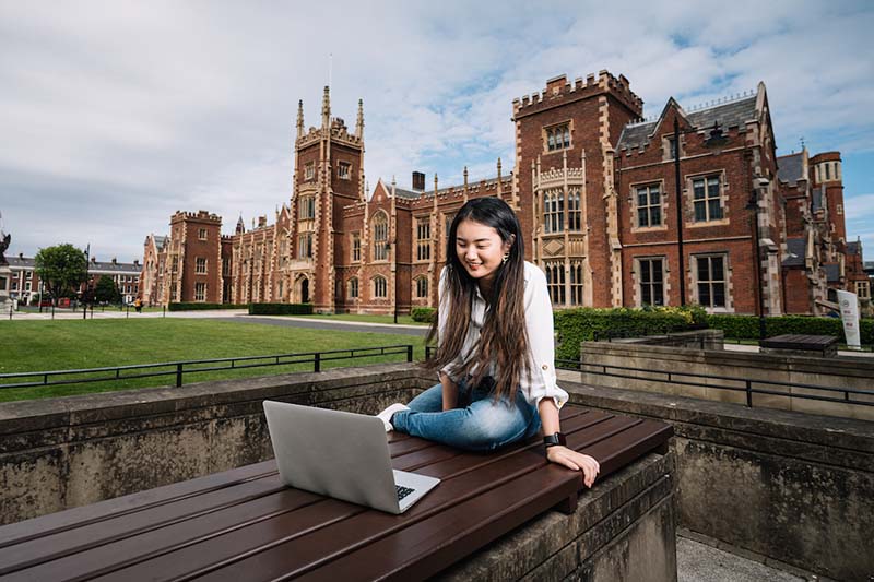 Student on laptop in front of Lanyon