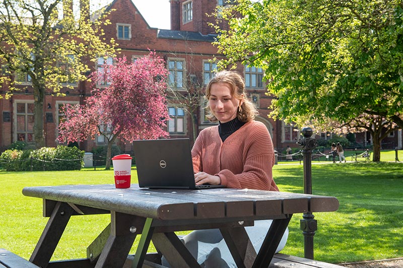 Tessa Rendina at a picnic table int he quad on a laptop