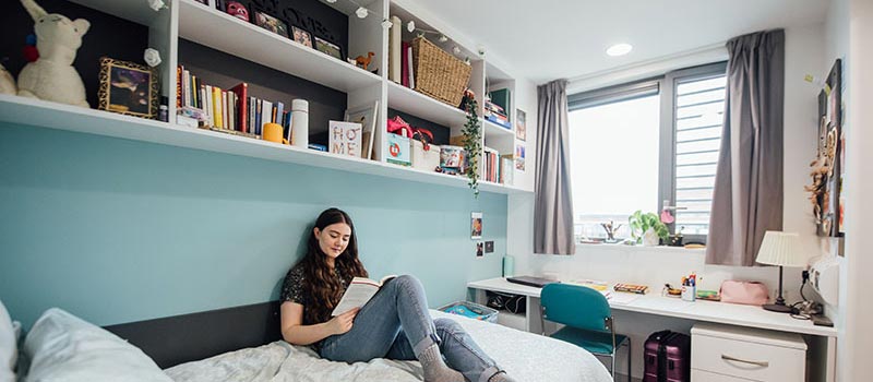 Student sitting on her bed in Queens accommodation