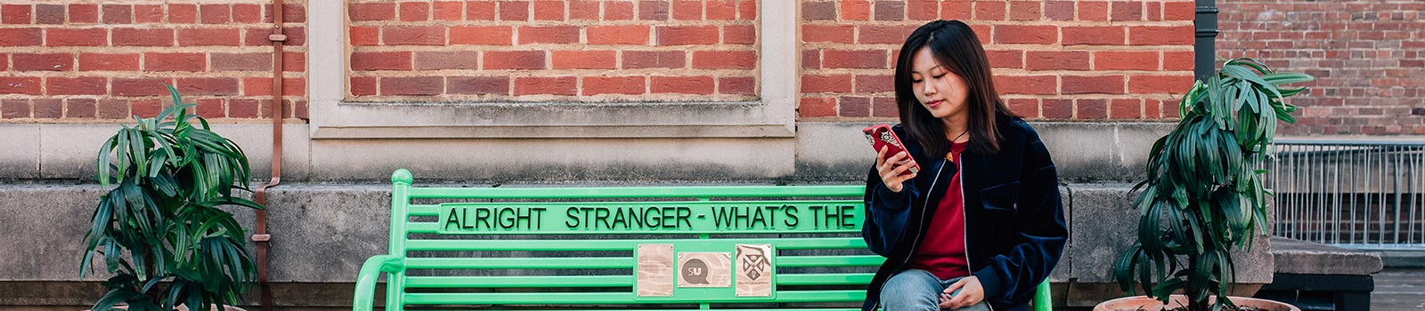 Student on a phone, sitting on a green bench