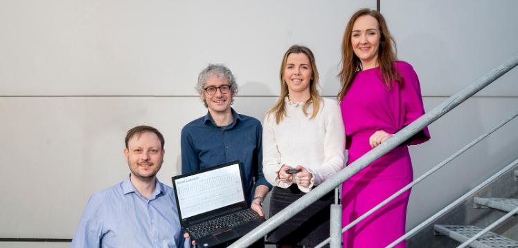 Four people standing on stairs holding a laptop