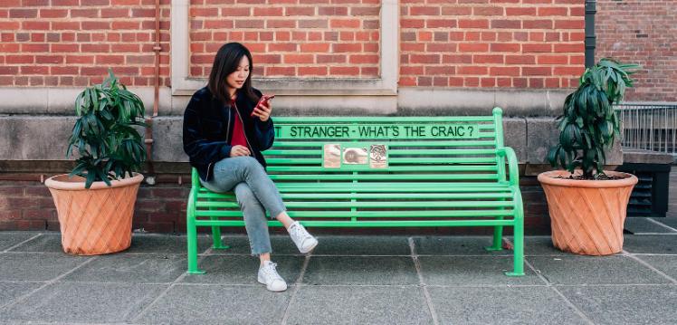 Sijin sitting on a bench that says Whats the craic