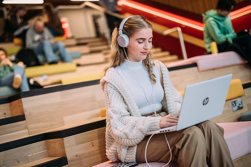 Student on a laptop with headphones sitting on the stairs in One Elmwood