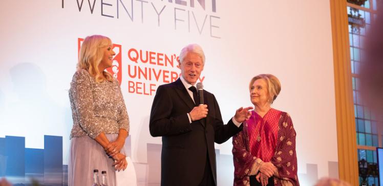 Three people stand in evening dress and the man holds a microphone