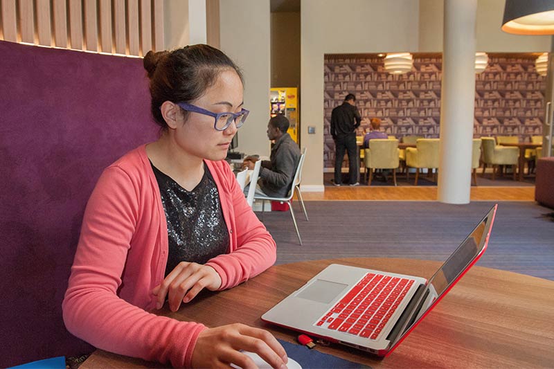 Female international student using laptop in coffee shop