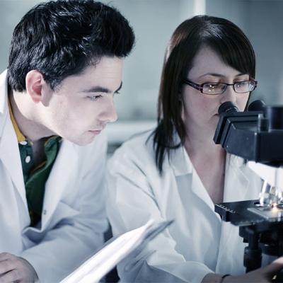 female student looking in to microscope with male student taking notes