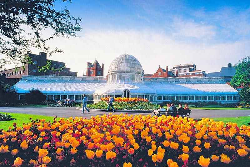 a bed of red and yellow flowers with the Botanic gardens Palm house in the background