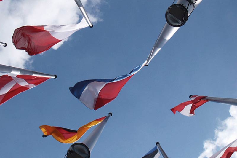 Multiple national flags flying beneath a blue sky