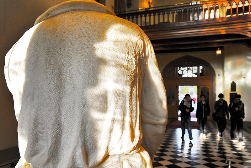 back of galileo statue with students walking through the black and white hall in the background