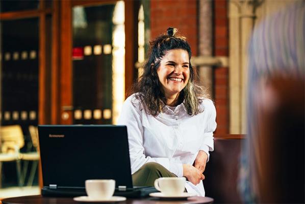 smiling female student sitting in the Graduate school with a laptop and a cup of coffee in front of her