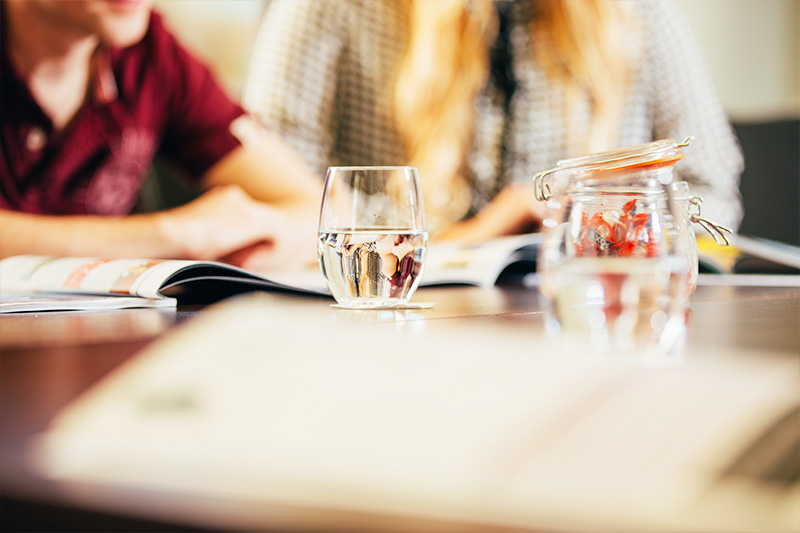 close up of a meeting room table with glasses on it and students in the background