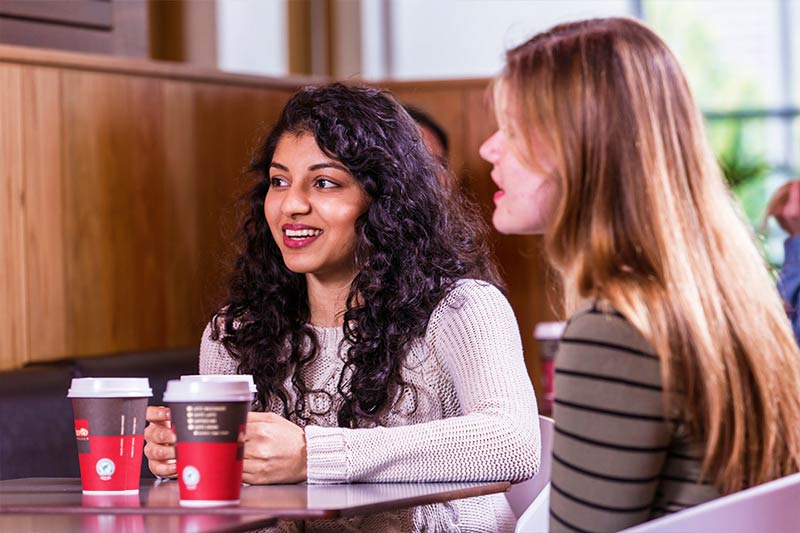 close up of two female students drinking coffee in the Treehouse Area of Elm's Village student accommodation