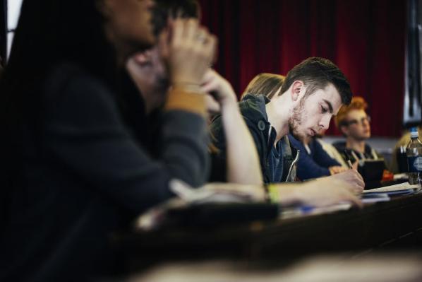 male student taking notes with other students in foreground