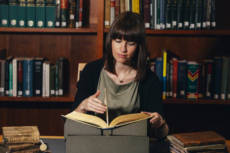 female student turning the page of an old journal, supported by a book holder