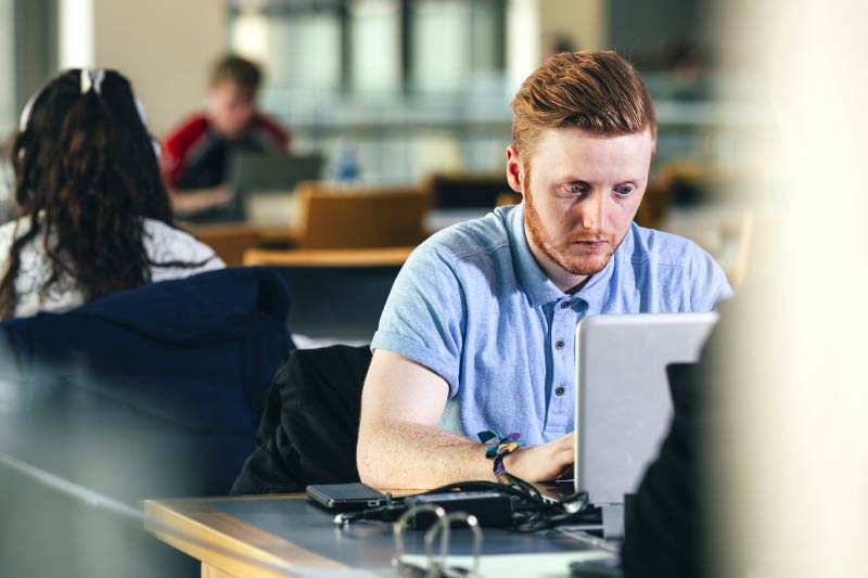 close up of red-headed male student working on a laptop