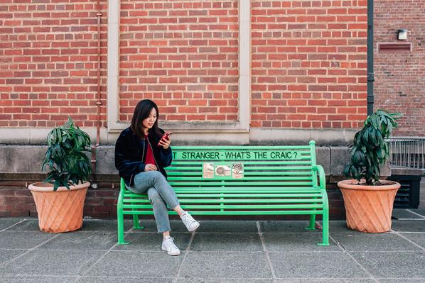 A student seated on a green bench outside the Students' Union building