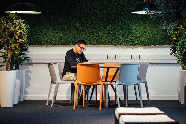 A student writes at a table with colourful chairs in the Computer Science Building