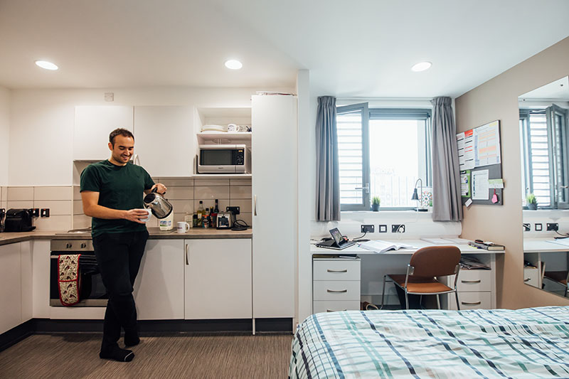 Male student making tea in studio apartment